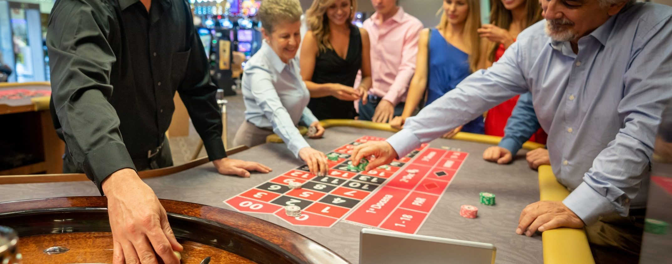 Casino worker ready to release the ball on the roulette wheel while others are still placing bets on table smiling